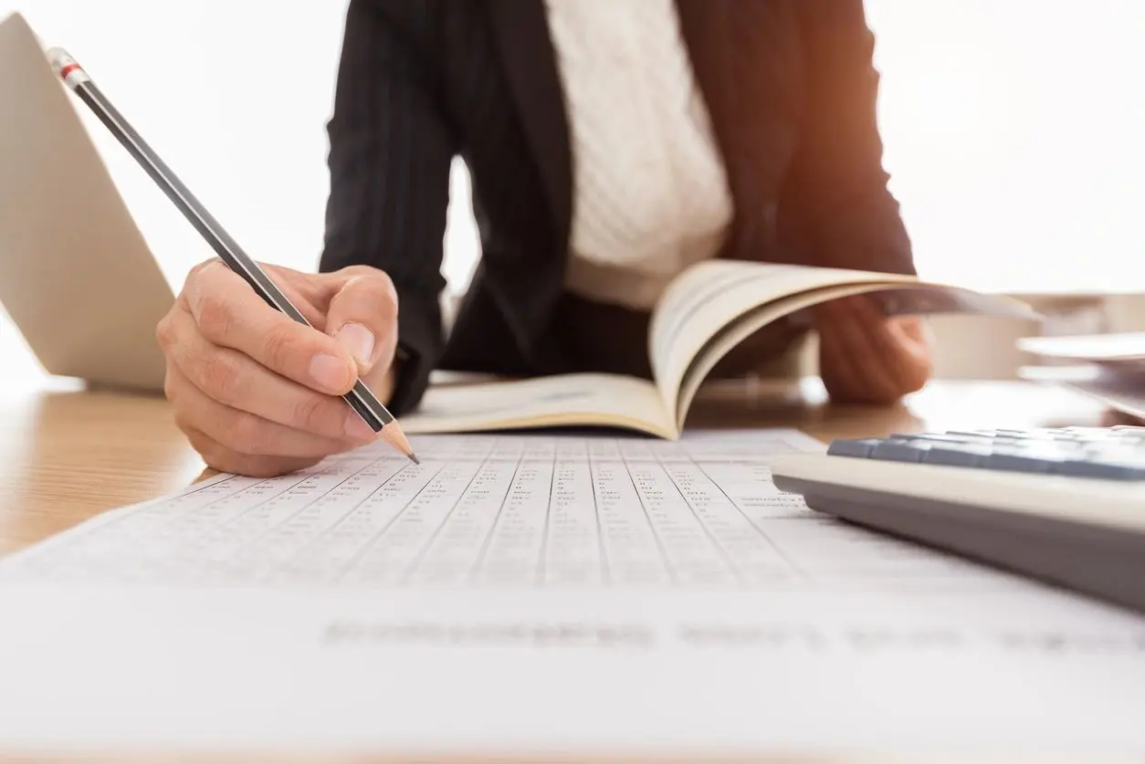 A person writing on paper with a pen and calculator.