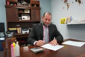 A man in suit and tie sitting at a table writing on paper.